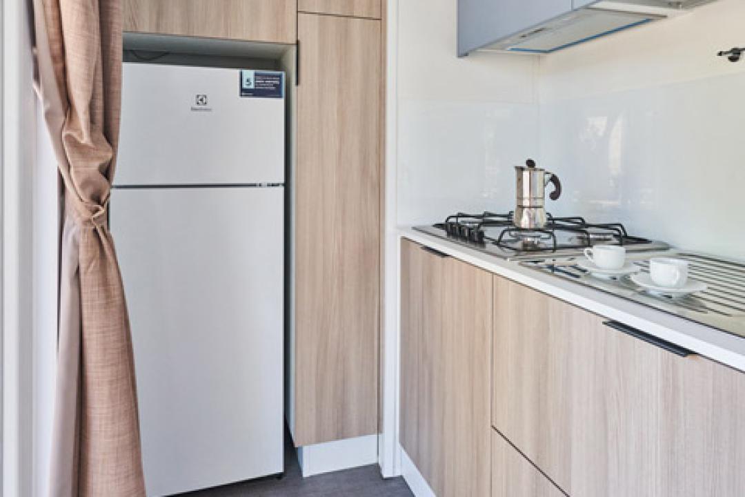 Cucina moderna con armadi in legno, frigorifero e piano cottura a gas.