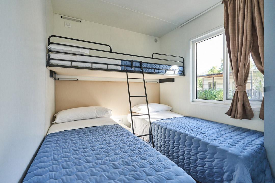 Zimmer mit Etagenbetten und Fenster, blaue Bettdecken.