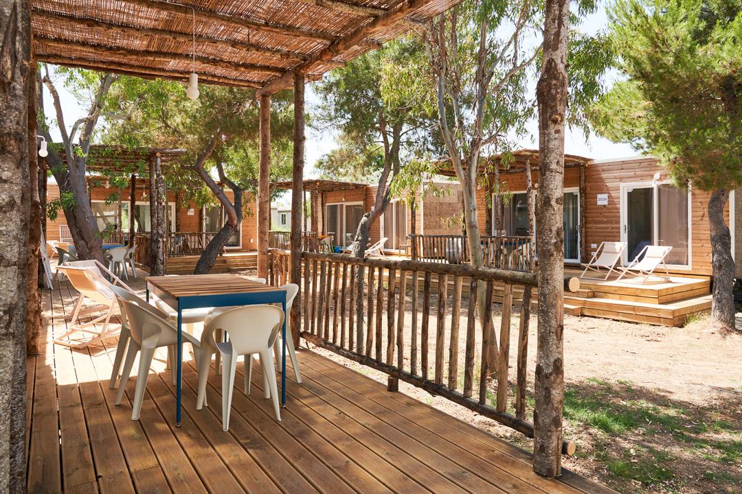 Houten terras met tafel, stoelen en uitzicht op bungalows omgeven door natuur.